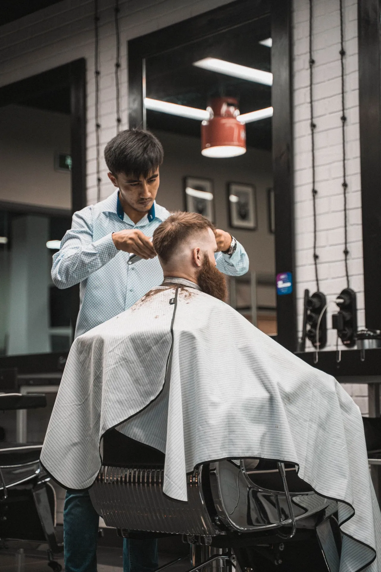 Un barbero trabaja con tijeras en un corte, junto a un espejo.