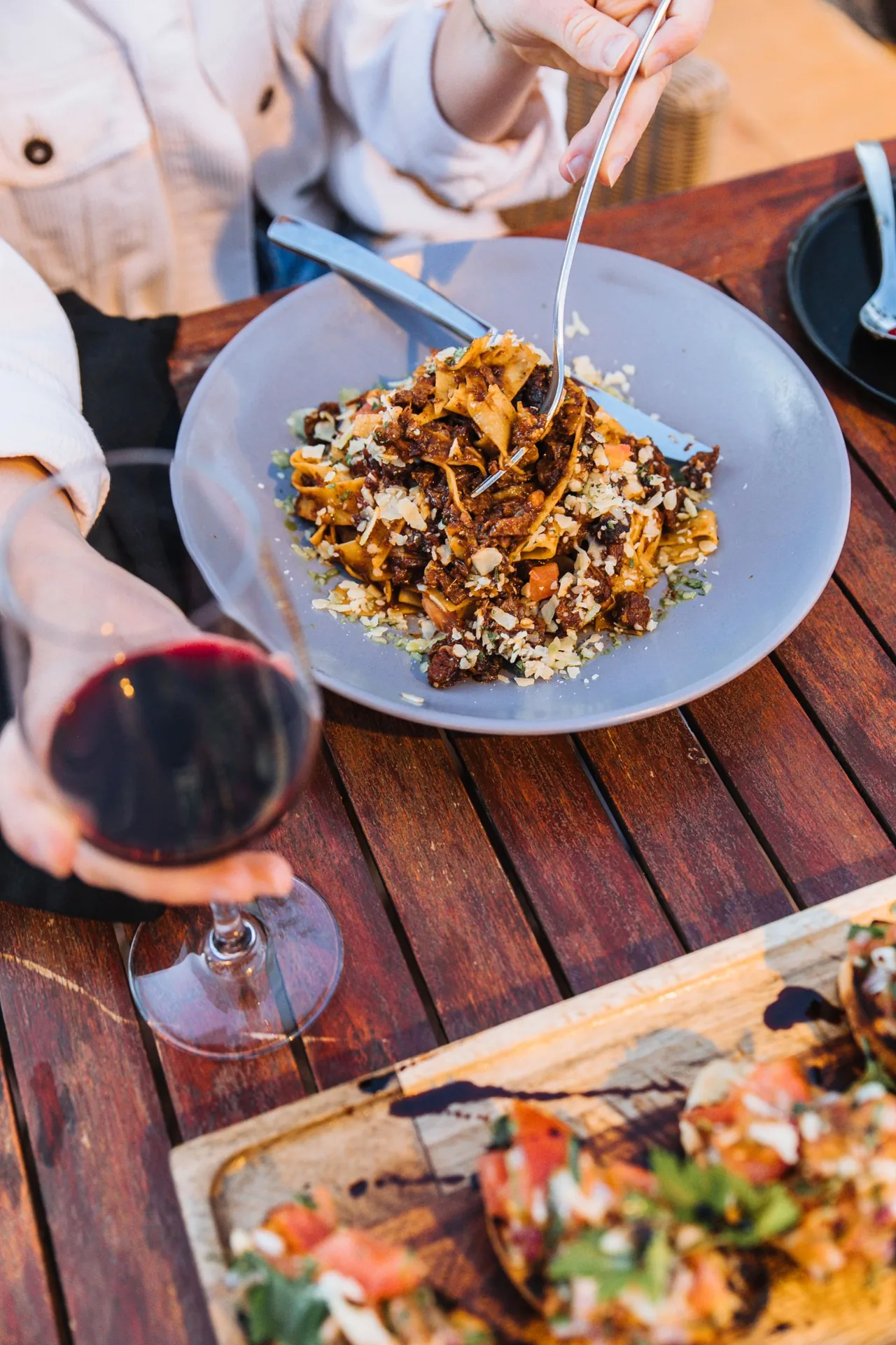 Pasta, copas de vino y una mesa de madera compartida; fotografía de ambientación.