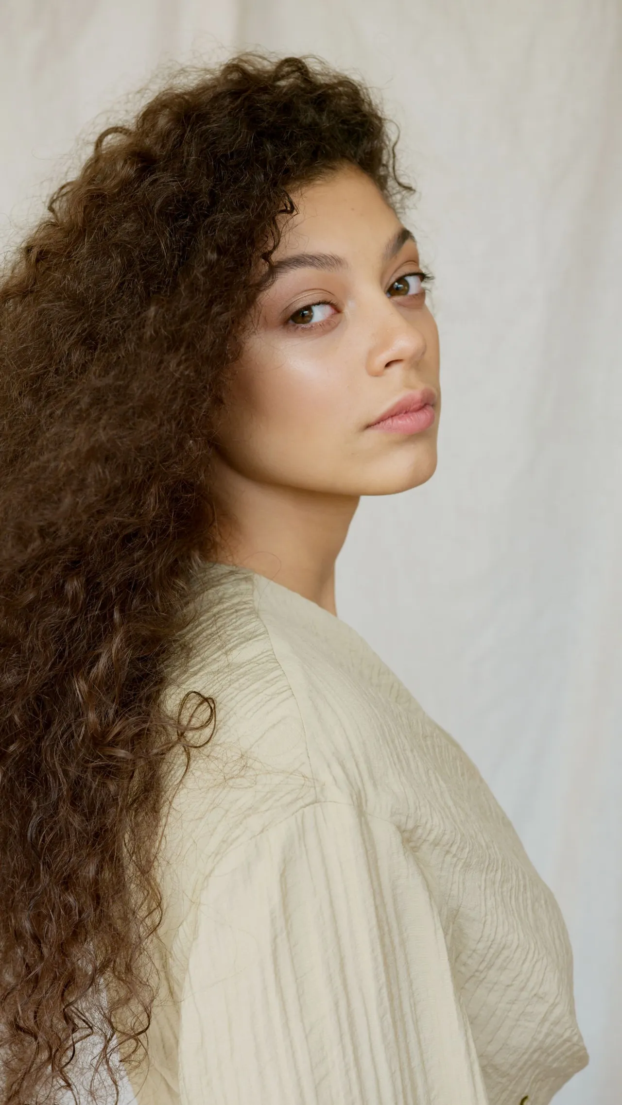 Retrato de una mujer con cabello rizado y voluminoso, sobre fondo claro.