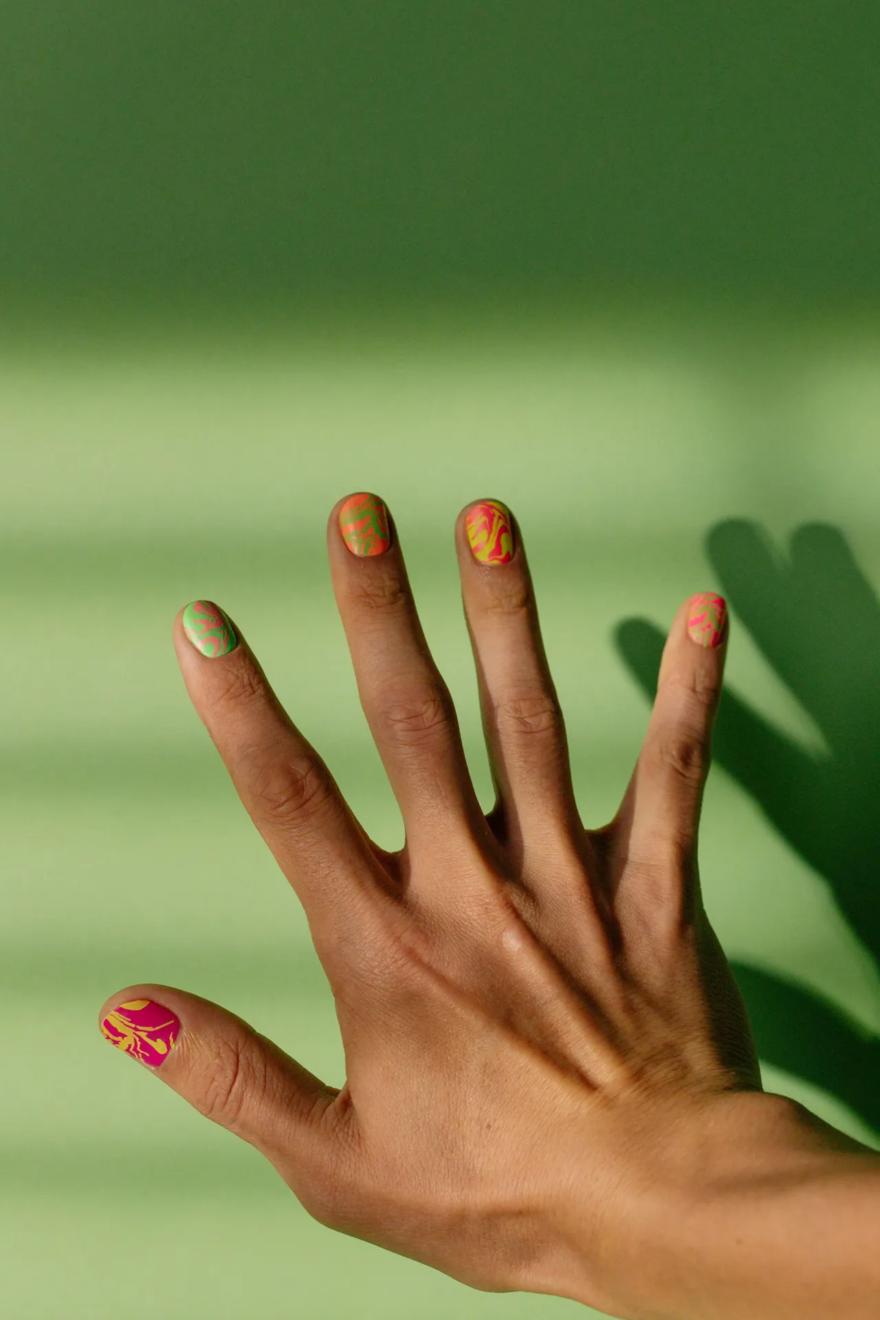 Mano con uñas decoradas con líneas de colores sobre un fondo verde.