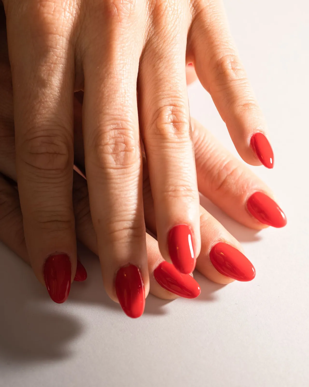 Manos con uñas pintadas de rojo sobre un fondo claro.